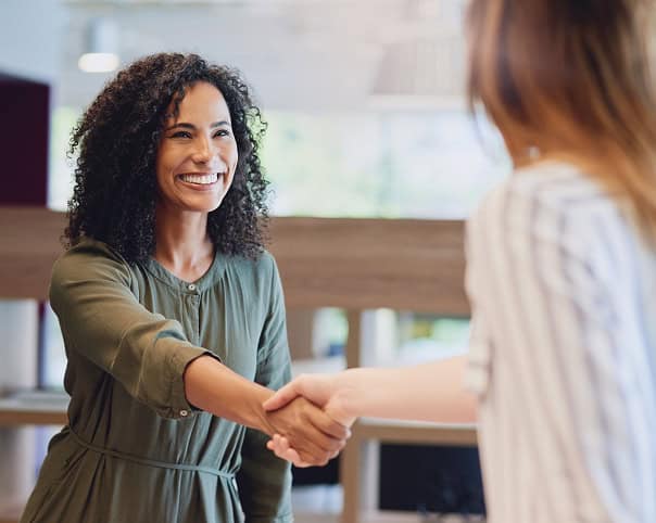 Profissional sorridente cumprimentando cliente com aperto de mão, ambiente corporativo e cordial no escritório.