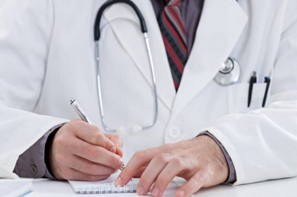 Profissional de saúde escrevendo em papel com estetoscópio ao pescoço para serviços médicos e jurídicos.