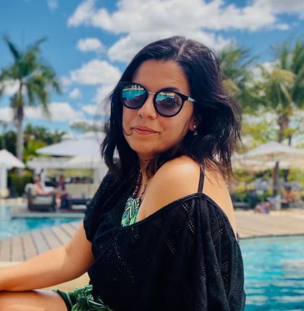 Praia com palmeiras, mulher de óculos escuros sorrindo, ambiente de lazer e descanso ao ar livre.