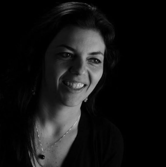 Rosto de mulher sorridente em luz baixa, expressão confiante e amigável.