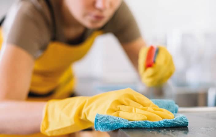 Limpeza doméstica com luvas amarelas e pano de microfibra, pessoa cuidando da higiene da casa.